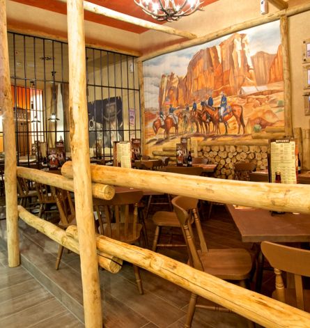 Arredamento su misura per ristorante stile western, tavoli e sedute in legno, staccionate e sbarre di metallo